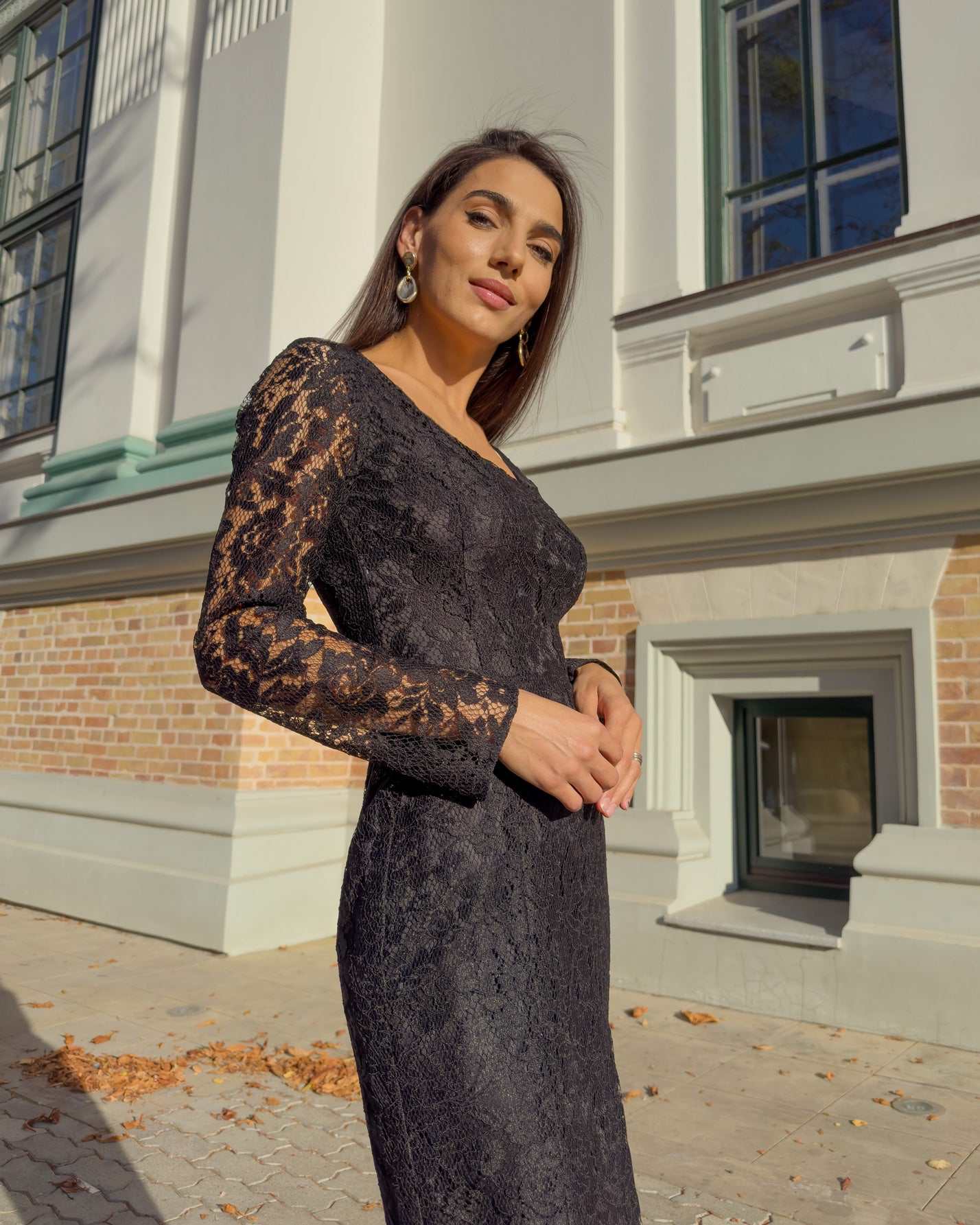 Rochie neagra din dantelă cu mâneci lungi și decolteu mic, ajustată pe corp.