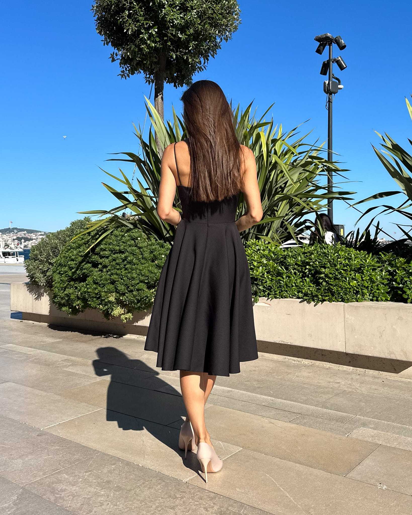 Rochie neagra elegantă scurtă cu bretele și fustă evazată în decor urban.