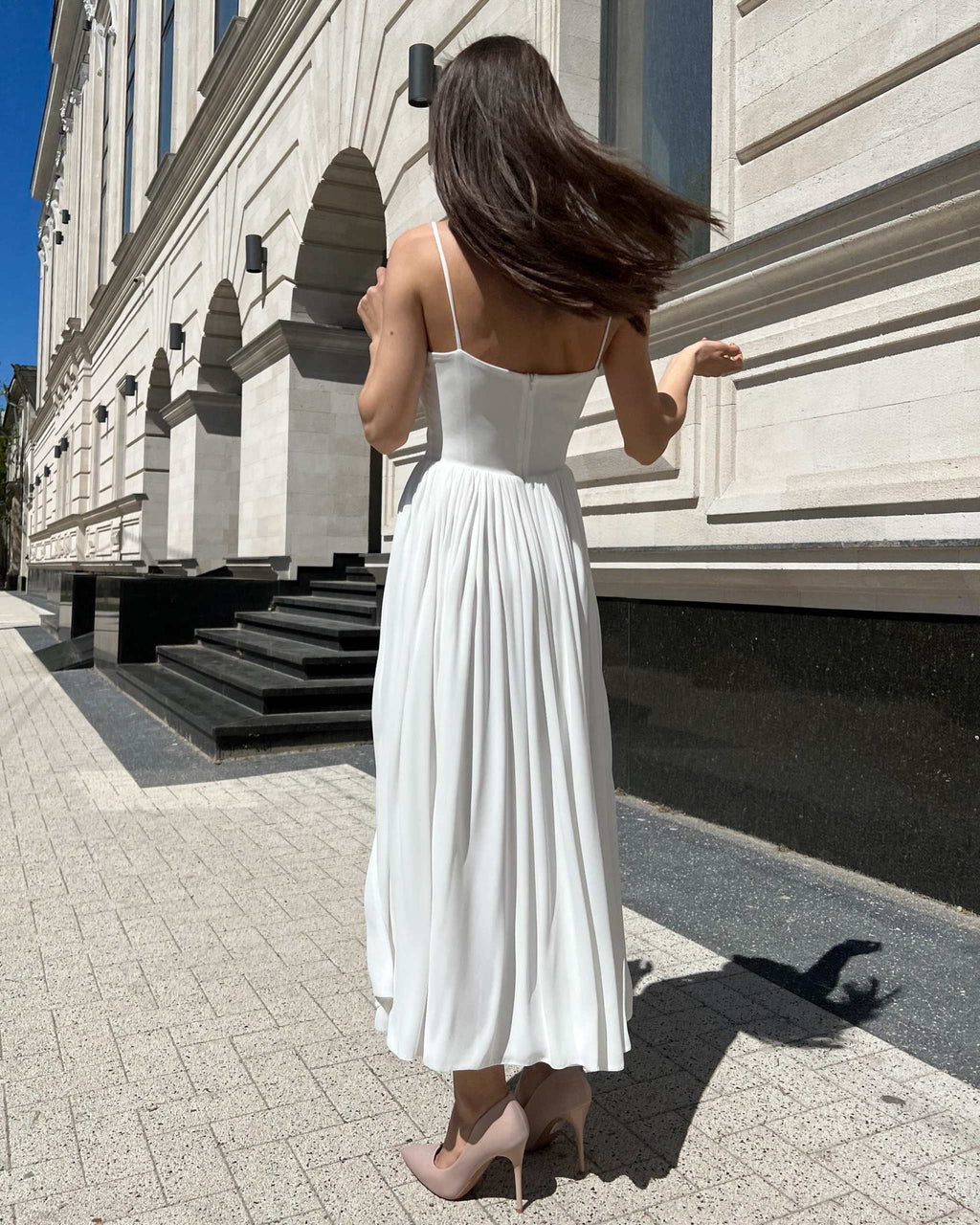 Rochie alba elegantă cu bretele și slit, lungime midi, accesorizată cu centură.