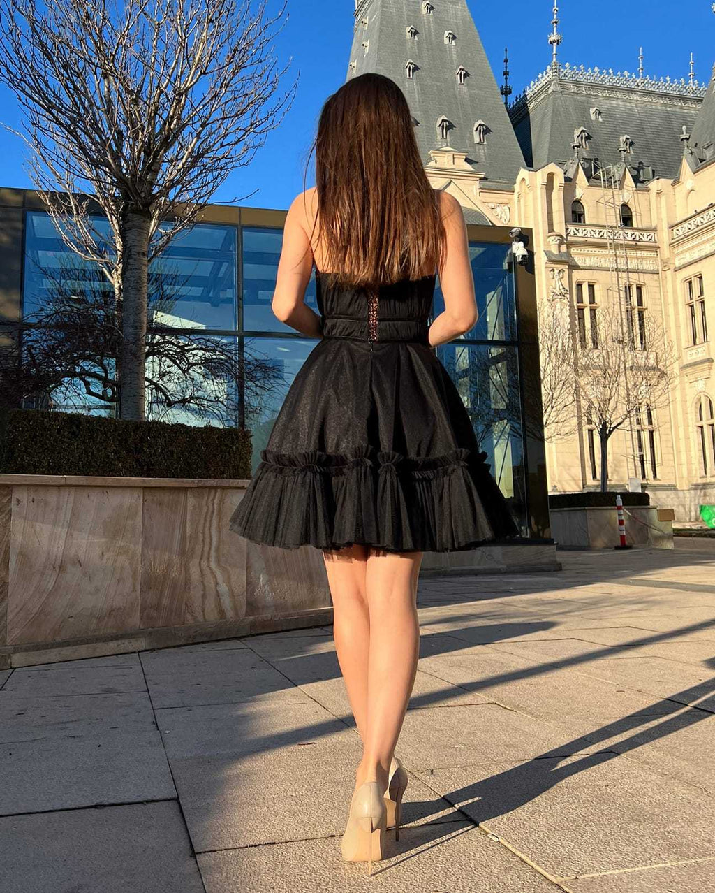 Rochie cocktail elegantă scurtă cu corset negru și fustă evazată, vedere din spate, în fața unui castel.